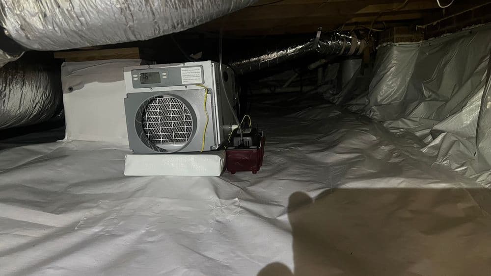 Dehumidifier operating in a residential crawl space with white vapor barrier.