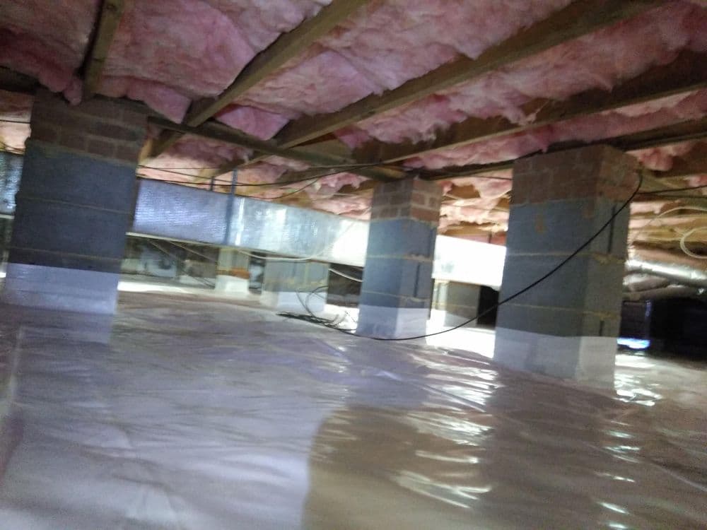 Crawl space insulation with pink fiberglass, concrete pillars, and plastic vapor barrier.