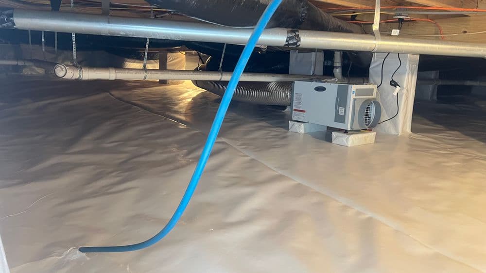 Crawl space with plastic lining, ventilation system, and blue tubing for moisture control.