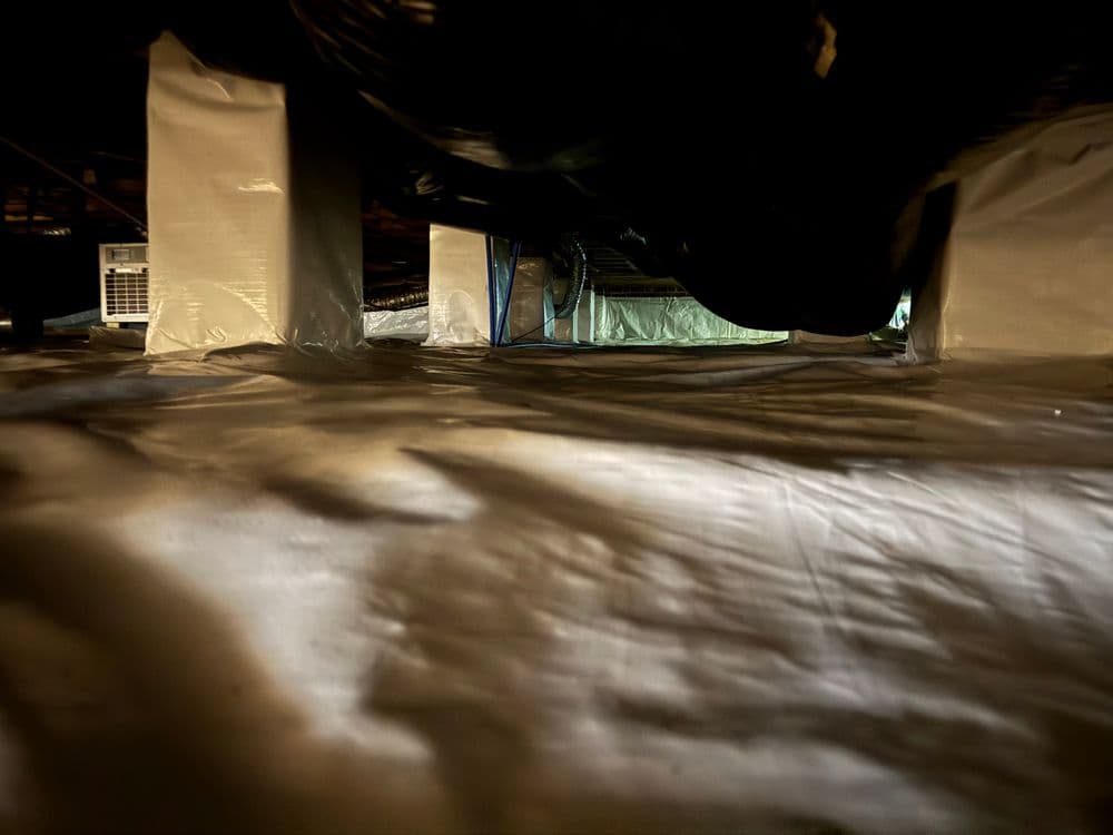 View of a dark crawl space with plastic barriers and ventilation equipment.