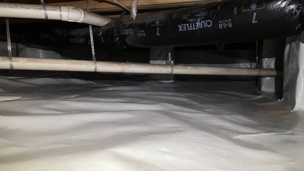 Crawl space with insulation and plumbing pipes, featuring a sealed plastic barrier on the ground.