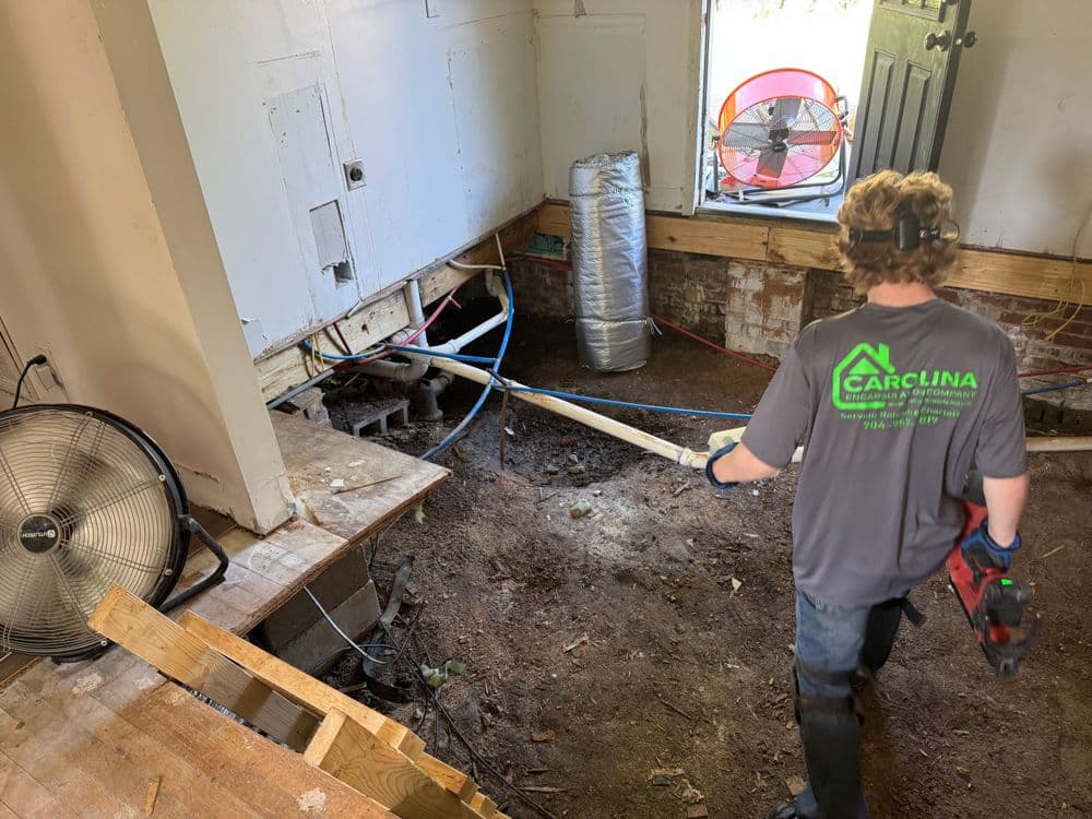 Worker repairing floor in a home renovation, exposing plumbing and electrical systems.