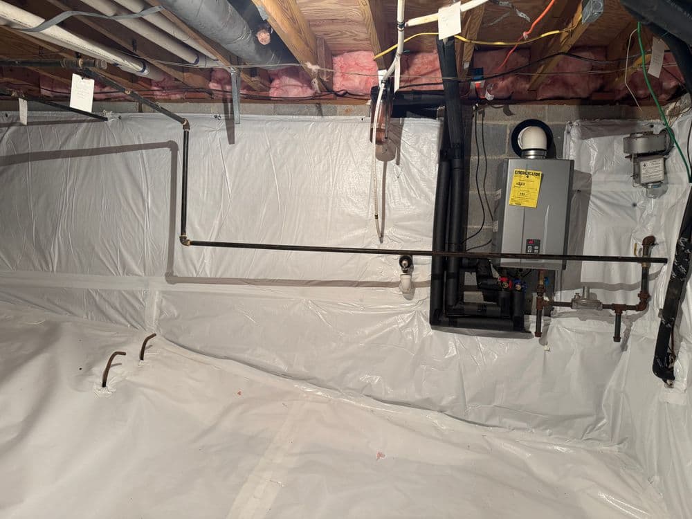 Basement installation with plumbing and heating system, featuring white plastic sheeting.