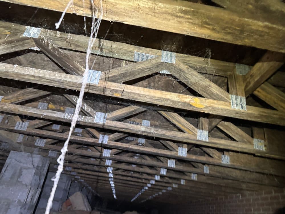 Detailed view of a wooden truss system in a dimly lit attic, showcasing structural support.