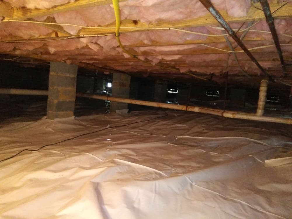 Crawl space with insulation and plastic sheeting, showing signs of moisture accumulation.